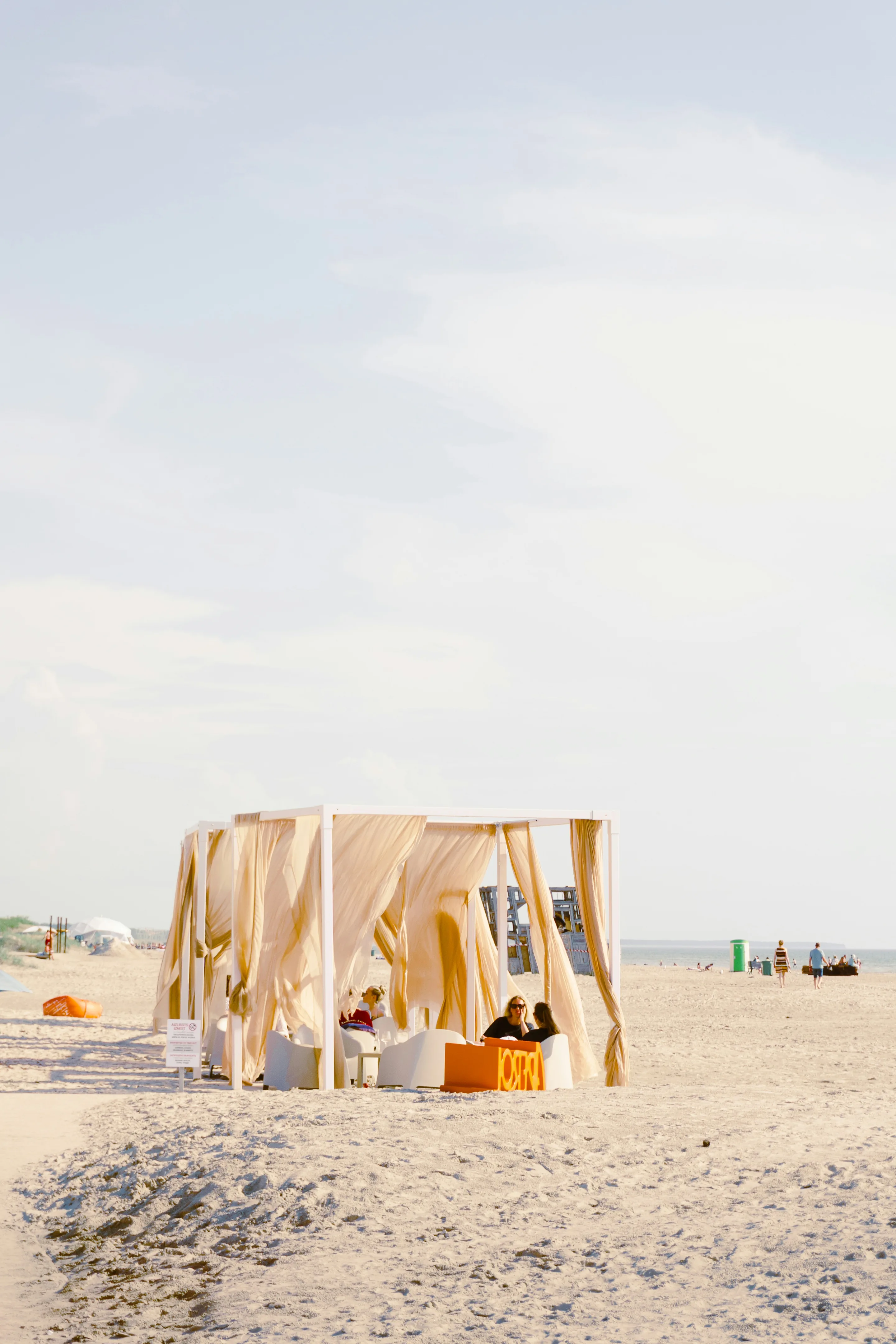 A cream fabric-draped cabana on pale sand under a wide sky