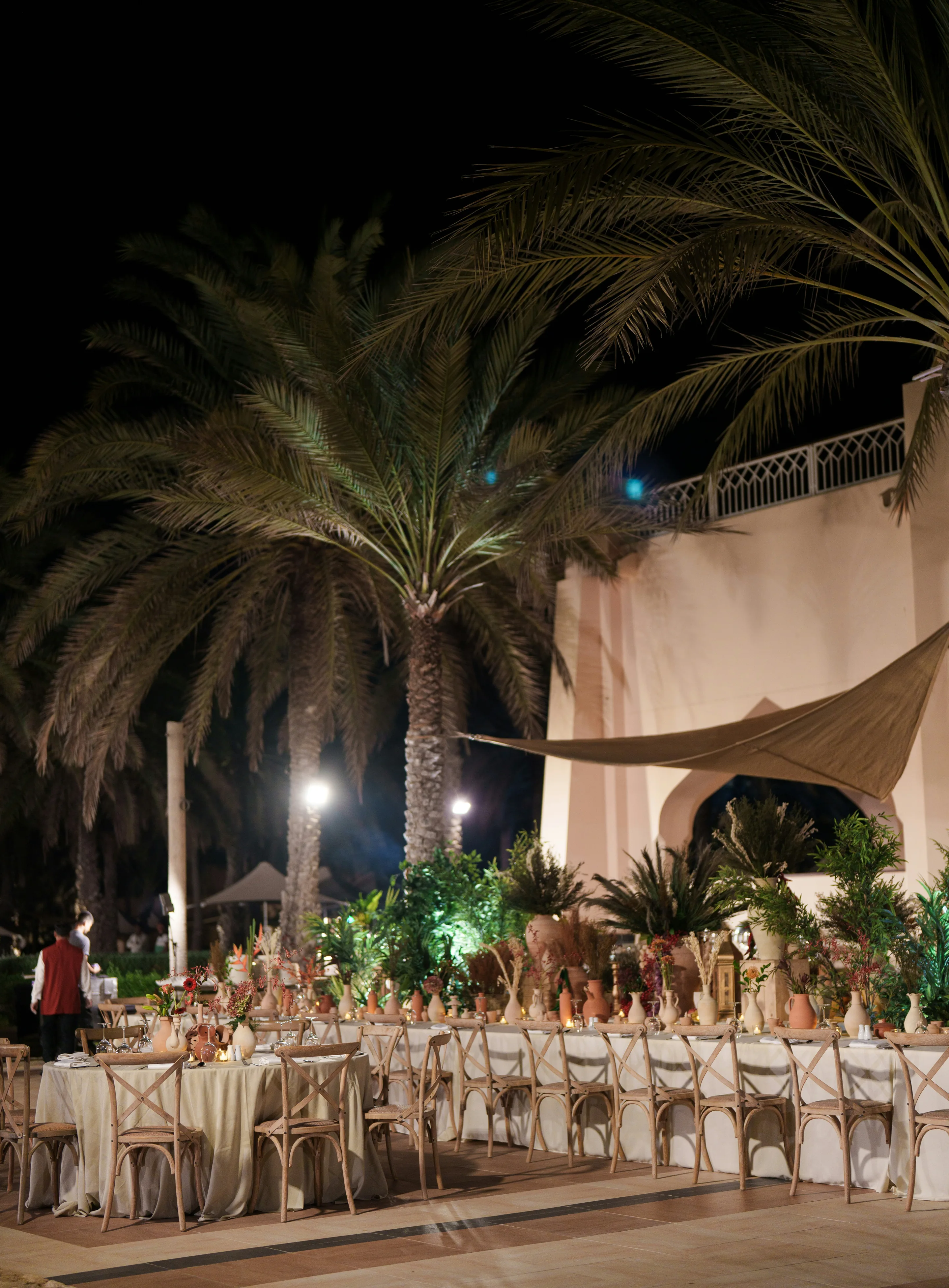 A long dressed table set outdoors at night beneath palms