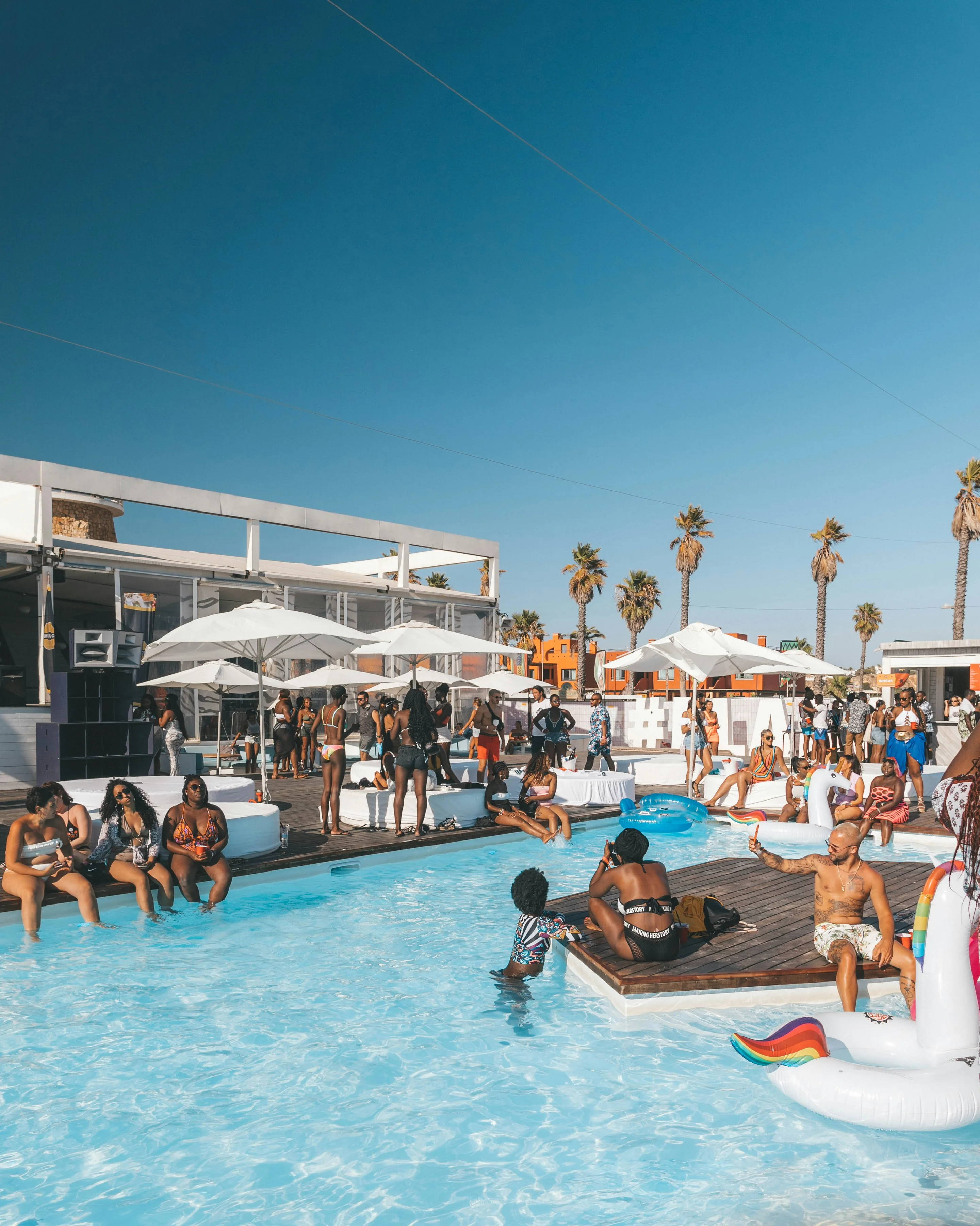 Guests relaxing in and around a turquoise pool under white parasols