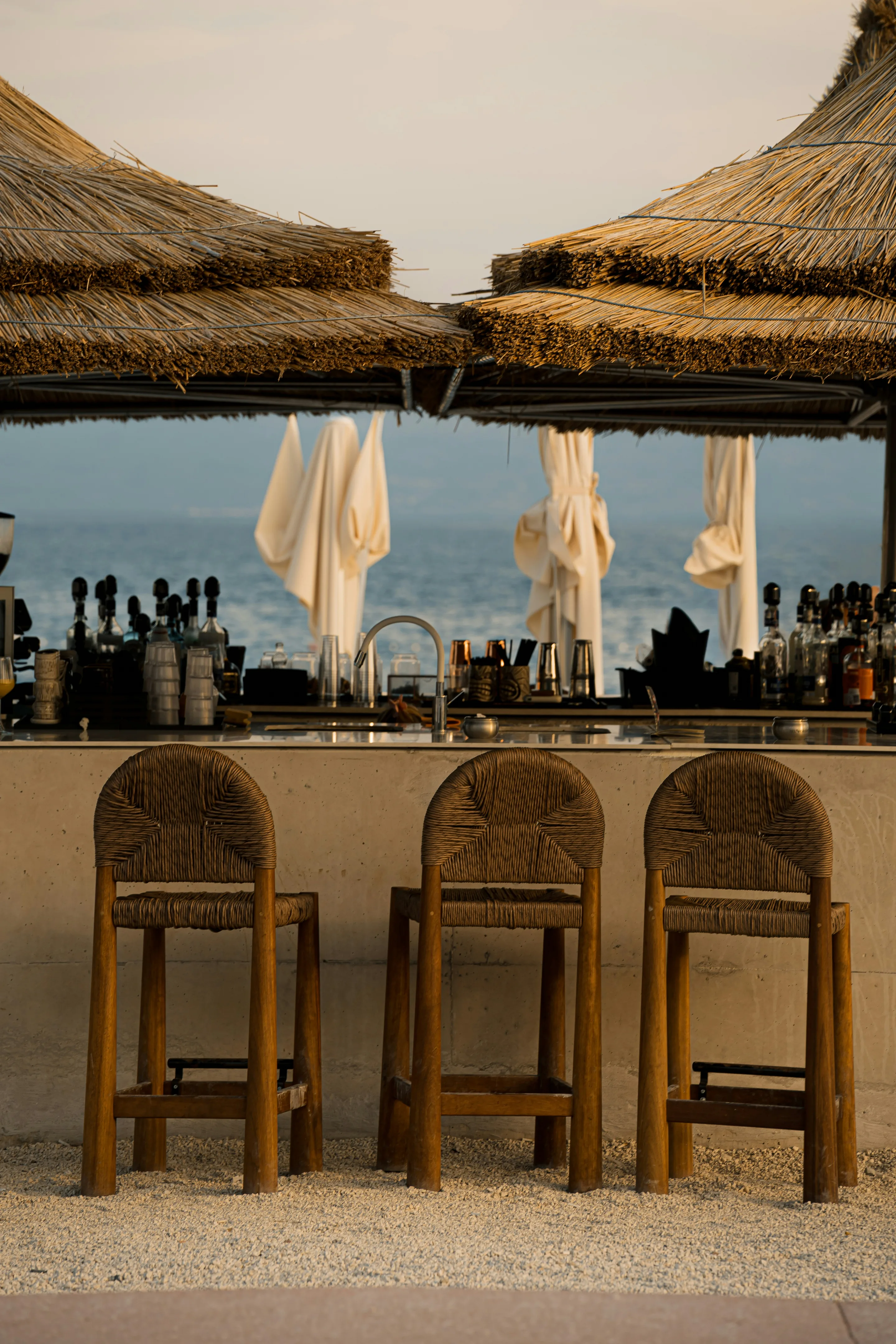 Woven wooden stools at a beach bar under thatched umbrellas